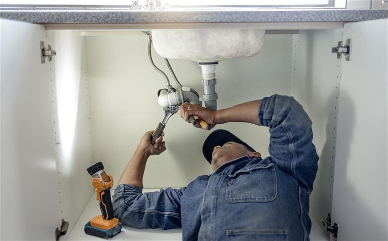 Plumber repairing pipes beneath a bathroom sink in Waco