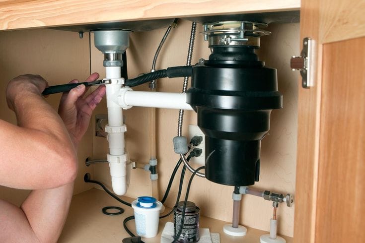 Plumber installing a garbage disposal beneath a kitchen sink in Waco