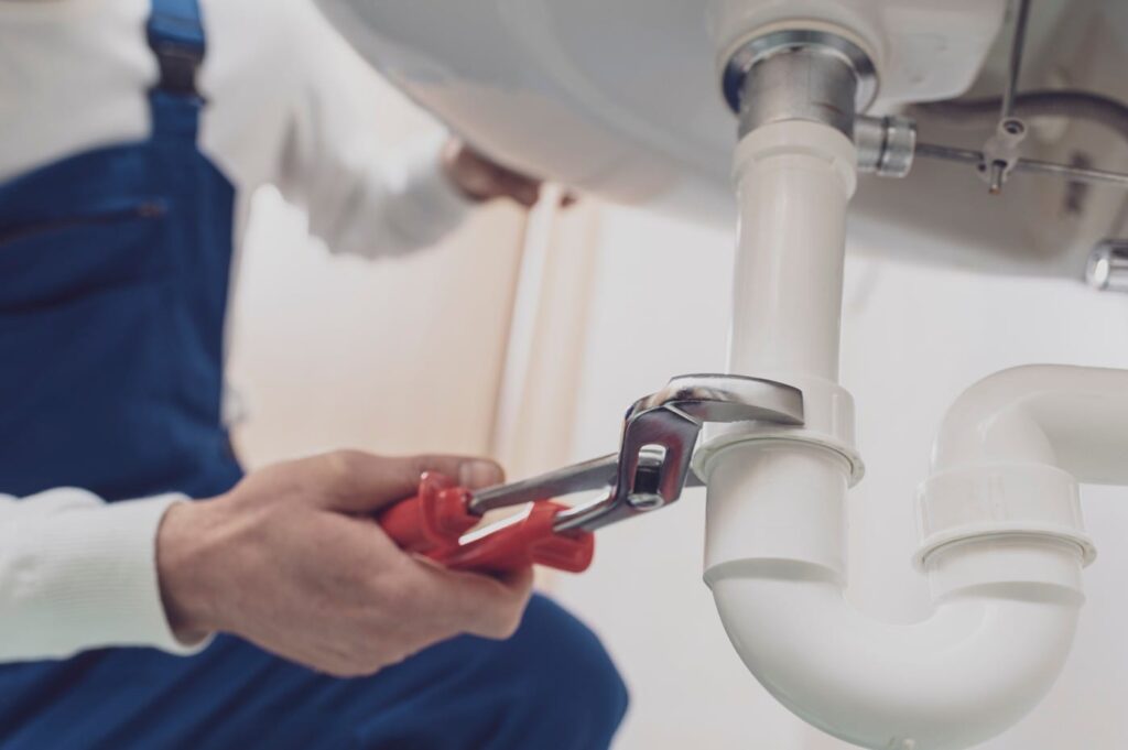 Plumber repairing a white drain pipe beneath a sink in Waco