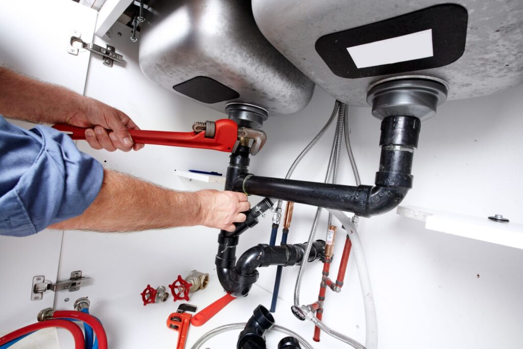 Plumber repairing drain pipes beneath a kitchen sink in Waco